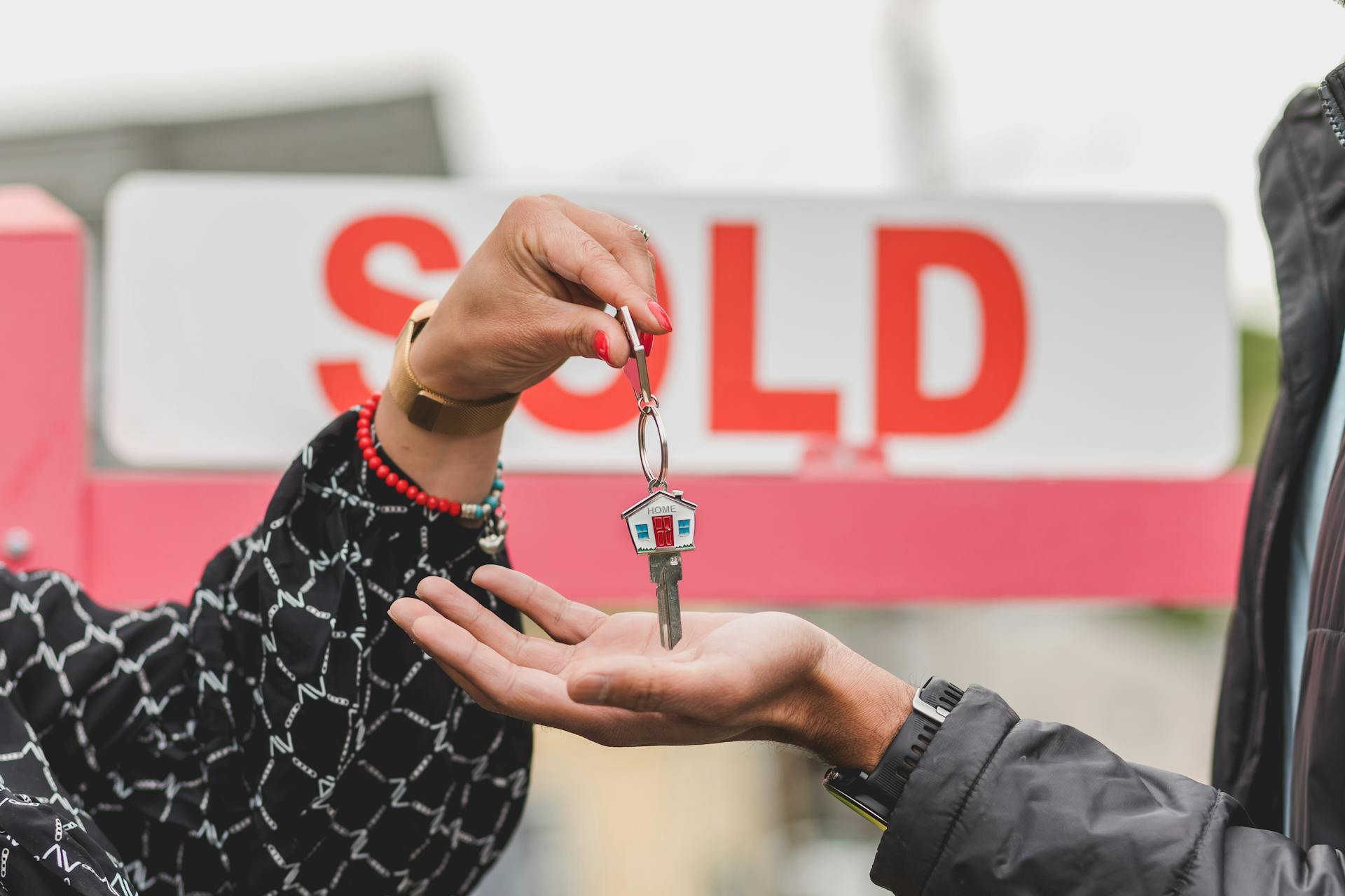 Schlüsselübergabe vor „Sold“-Schild – Symbol für erfolgreichen Immobilienverkauf oder Eigentümerwechsel.