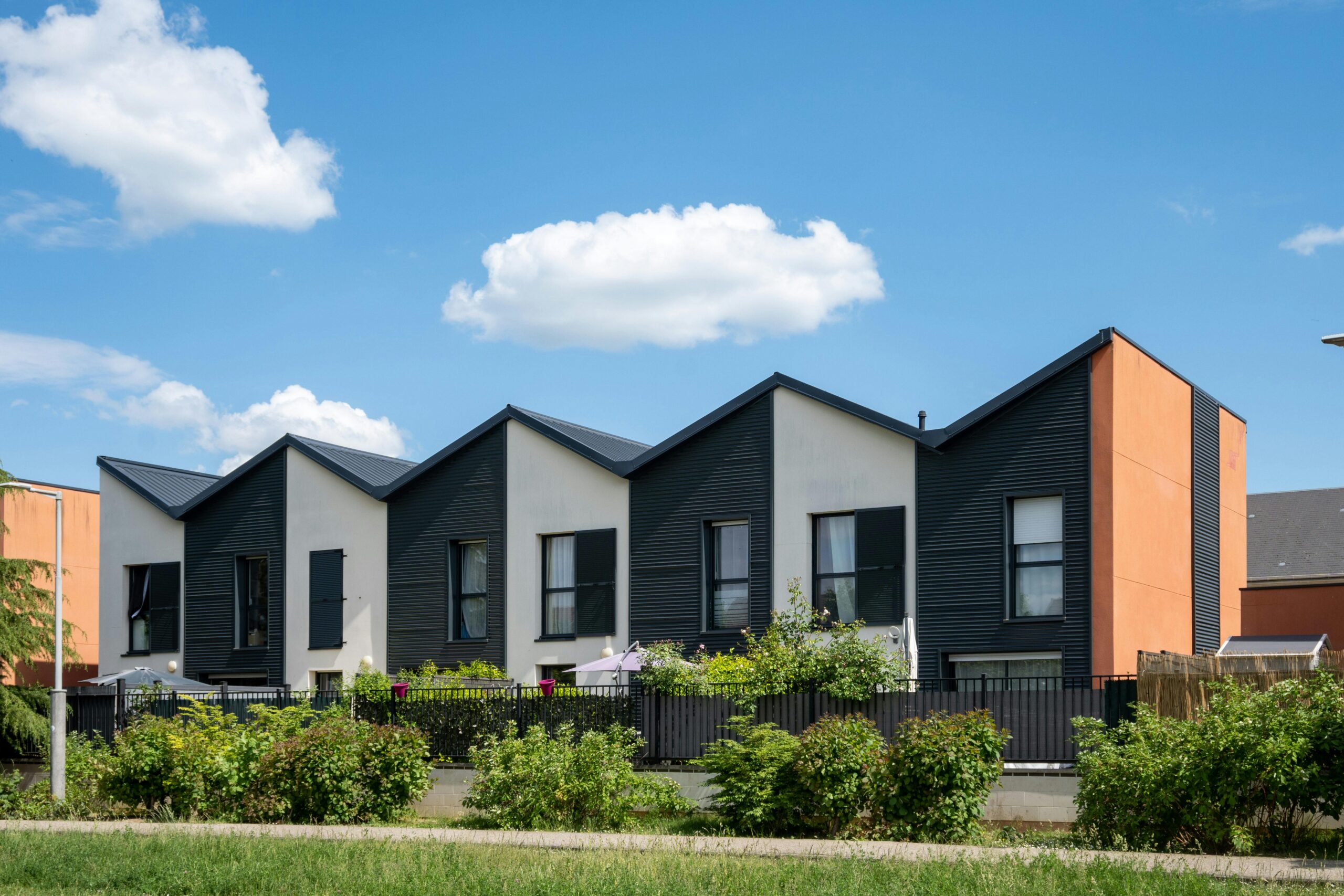 Modulares Wohnen - Moderne Reihenhäuser mit Gartenumzäunung und blauem Himmel.
