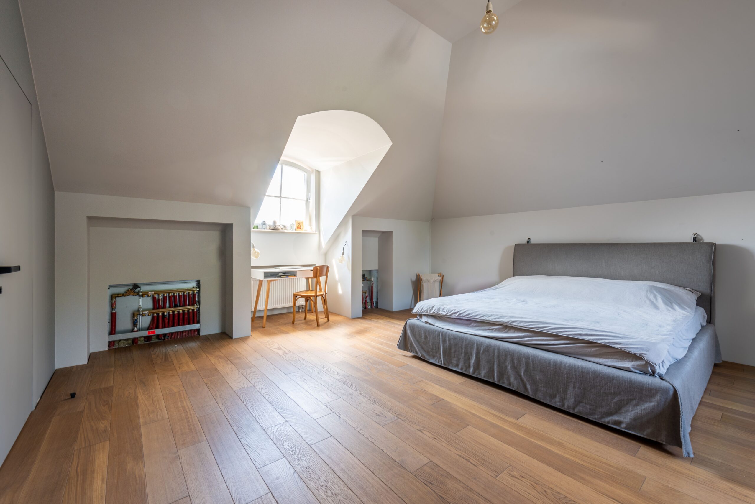 Helles Schlafzimmer im Dachgeschoss mit Doppelbett, Holzboden, Dachfenster und kleinem Arbeitsbereich